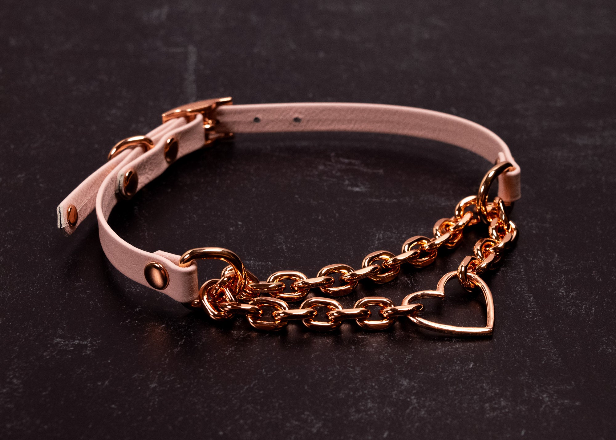 Pink leather choker with rose gold chain and heart charm on a dark background