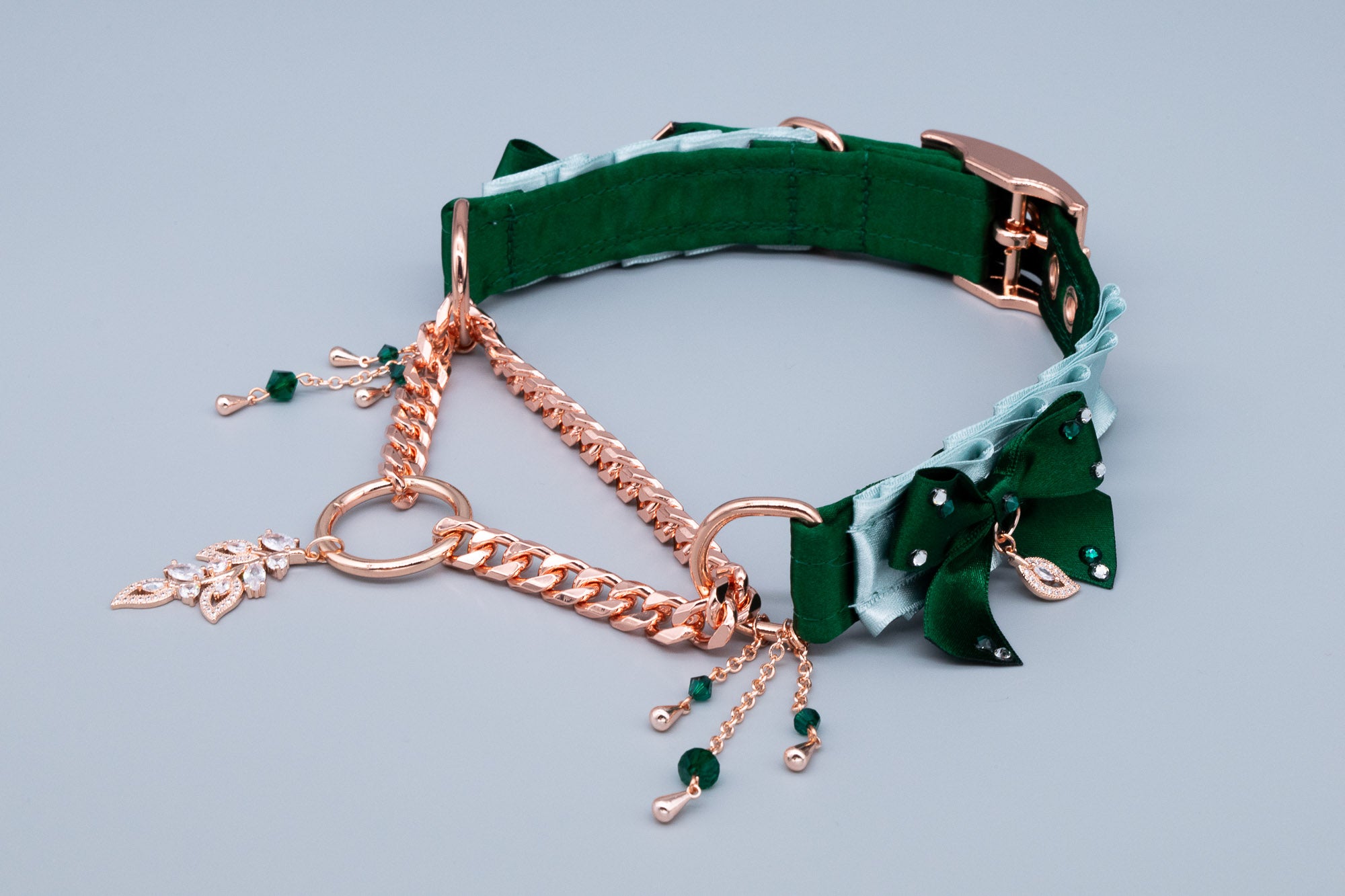 A hunter green and seafoam satin martingale collar with rose gold hardware and crystal embellishments, including a chain, bows, and a leafy pendant.